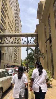 two women walking down the street in front of tall buildings with cars parked on both sides