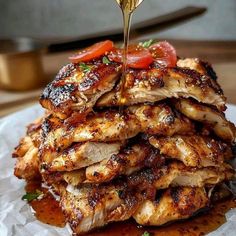 a pile of chicken with sauce being drizzled over it and topped with tomatoes