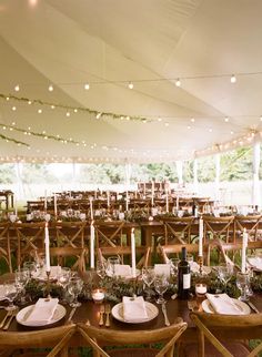 an outdoor tent with tables and chairs set up for a formal dinner or party, surrounded by string lights