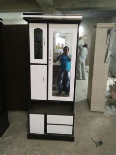 a woman taking a selfie in the mirror of a tall cabinet that is being constructed