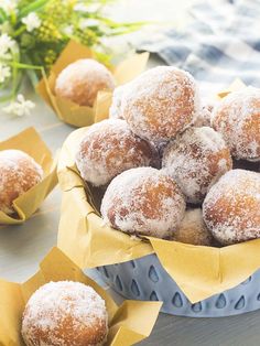 powdered sugar donuts in a blue bowl on a table with yellow napkins