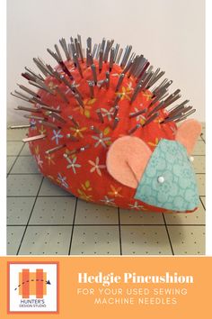 a red hedgehog pincushion sitting on top of a tiled floor with needles sticking out of it