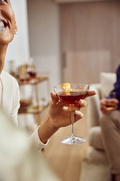 a woman holding a wine glass filled with red liquid and an orange peel in it