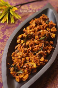 a wooden spoon filled with cooked food on top of a purple table cloth next to yellow flowers