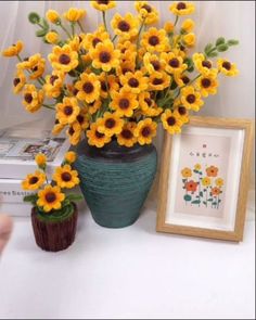 a vase with yellow flowers sitting next to a framed picture and small potted plant