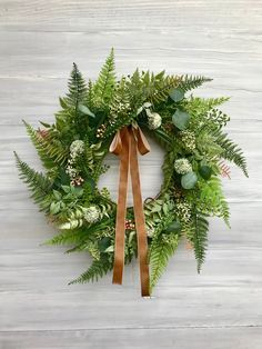 a green wreath with brown ribbon hanging on a white wooden wall, decorated with greenery and berries