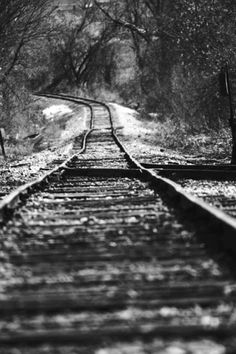 black and white photograph of train tracks in the snow with trees on either side,