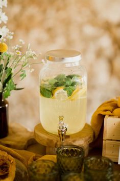 a glass jar filled with lemonade sitting on top of a table next to flowers