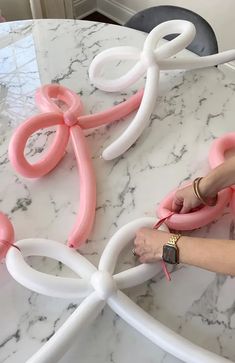 a woman is making balloon art with pink and white balloons on a marble table top