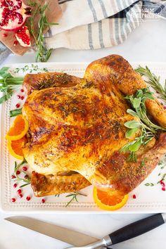 a roasted chicken with oranges and herbs on a plate next to a cutting board