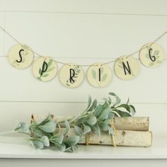 a white shelf topped with books and plants next to a string sign that says spring