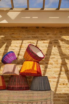 colorful lamps are on display in front of a brick wall under a skylight with shadows from the roof