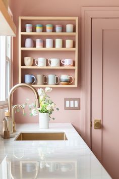 a kitchen with pink painted walls and white counter tops, gold faucet, open shelving above the sink