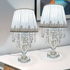 pair of crystal table lamps with white shades on top of the lamp and below them