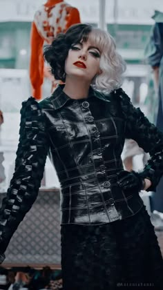 a woman with white hair wearing a black dress and red lipstick standing in front of mannequins