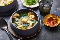 two bowls of soup with spinach and other foods on the table next to them