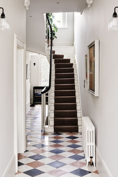 a hallway with stairs and tiled flooring next to a painting hanging on the wall