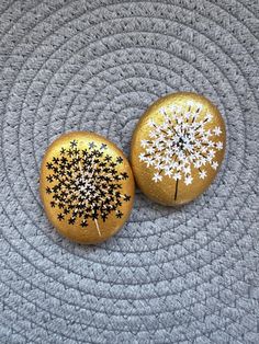 two painted rocks sitting on top of a gray rug next to each other, one with a dandelion design