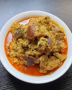 a white bowl filled with food sitting on top of a wooden table covered in sauce