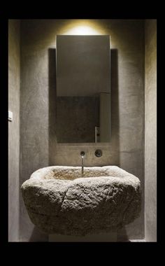 a stone sink in the corner of a room with a mirror above it and lights on