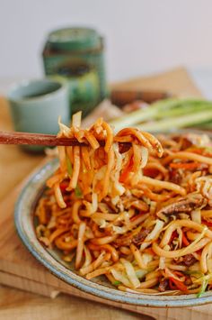 a plate full of noodles and vegetables with chopsticks sticking out of the bowl