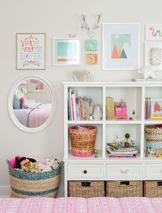 a white bookcase filled with lots of books next to a pink bedspread