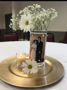 a vase filled with white flowers on top of a gold plate next to a candle