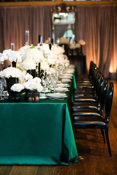 a long table is set with black chairs and white flowers in vases on it