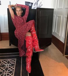 a woman in red boots is sitting on a black chair and posing for the camera