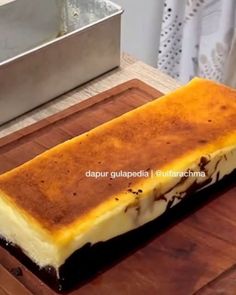 a piece of cheesecake sitting on top of a wooden cutting board next to a metal pan