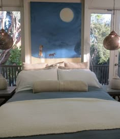 a bed with two lamps hanging from it's sides and a painting on the wall