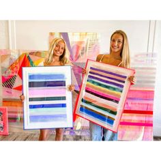 two women holding up art pieces in front of a wall with multiple color swatches