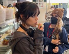 two women wearing face masks and eating food in a kitchen while looking at the camera