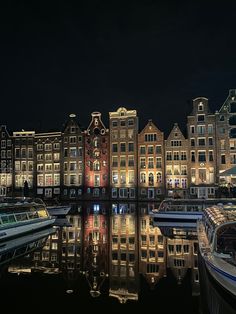 boats are docked in the water at night near some buildings and lights on their sides