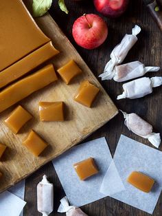 several pieces of caramel cheese are on a cutting board next to apples and garlic