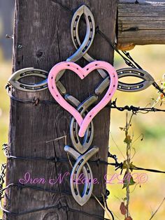 a heart shaped metal object hanging on a wooden fence post with barbed wire around it