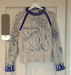 a white sweater with blue trims hanging on a door