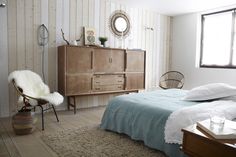 a bed room with a neatly made bed next to a dresser and chair in front of a window