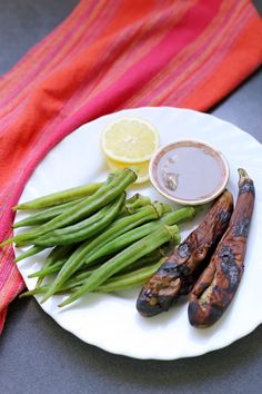 a white plate topped with green beans next to lemon wedges and an eggplant