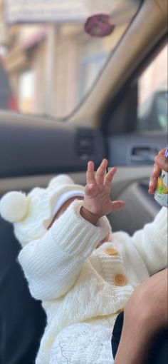 a baby sitting in the passenger seat of a car with its hand up to someone's head