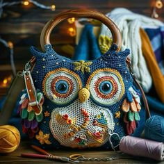 an owl purse sitting on top of a wooden table next to yarn and knitting needles