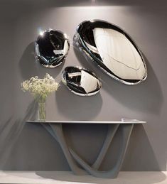 three mirrors on the wall above a table and vase with flowers in front of it