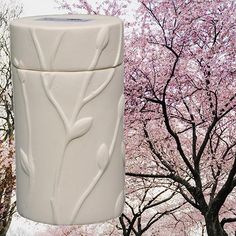 a white vase sitting next to a tree with pink flowers