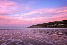 the sky is pink and purple over the water at the beach with waves coming in