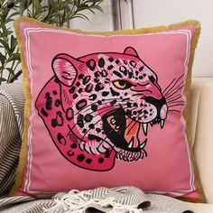 a pink leopard pillow sitting on top of a couch next to a potted plant