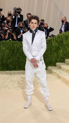 a man in a white suit and black tie standing on steps with cameras around him