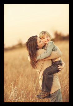 a woman holding a child in her arms while standing in the middle of a field