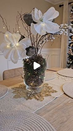 a glass vase filled with white flowers on top of a table next to a christmas tree