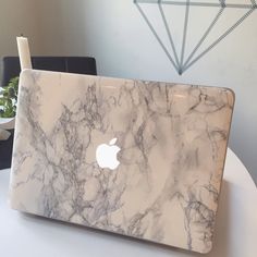 an apple laptop sitting on top of a white table next to a potted plant