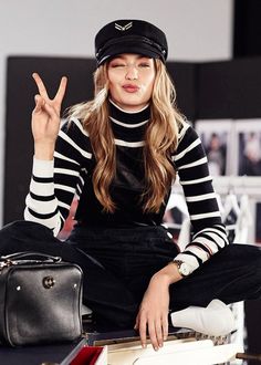 a woman sitting on top of a pile of suitcases holding up the peace sign